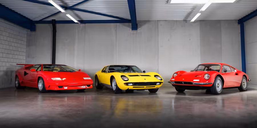 Červené Lamborghini Countach, žluté Lamborghini Miura a červené Ferrari stojí vedle sebe v hale