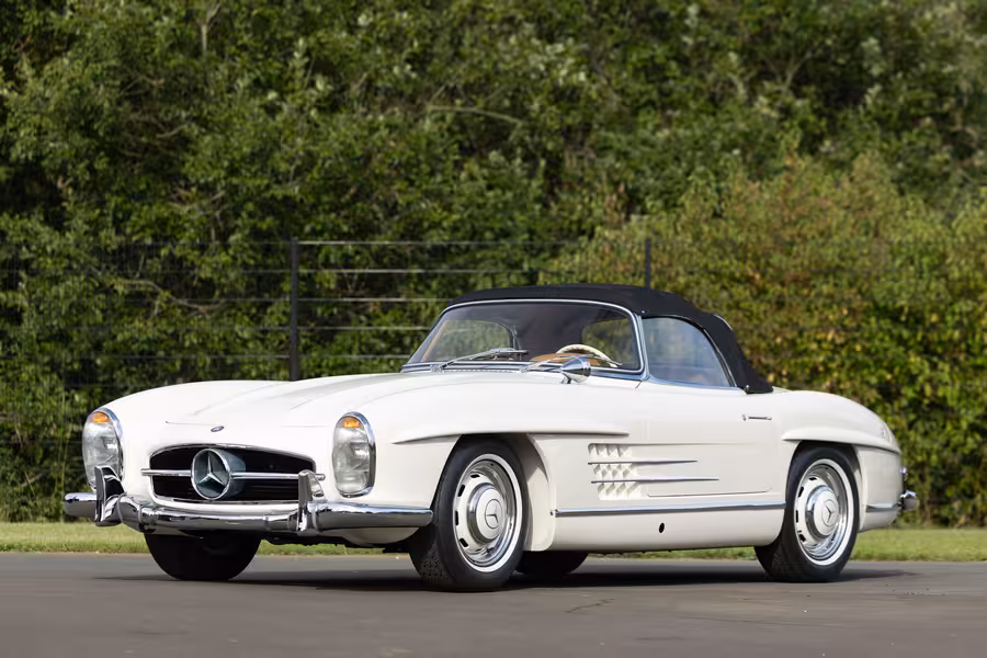 Bílý Mercedes-Benz 300 SL Roadster s černou plátěnou střechou stojí před zelení