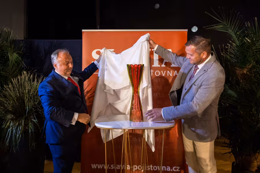 Dva muži odhalují vysokou červenou a zelenou skleněnou trofej na slavnostním večeru