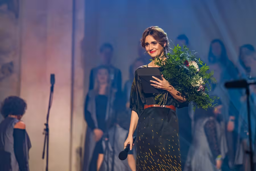 Daniela Brzobohatá stojí na pódiu s mikrofonem, tabletem a kyticí