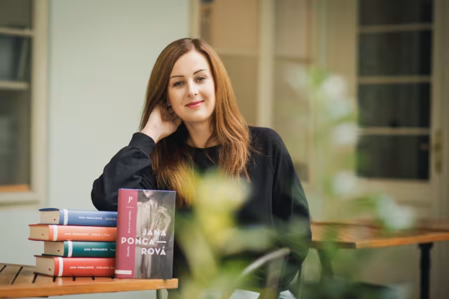 Jana Poncarová sedí u okna vedle stohu svých knih