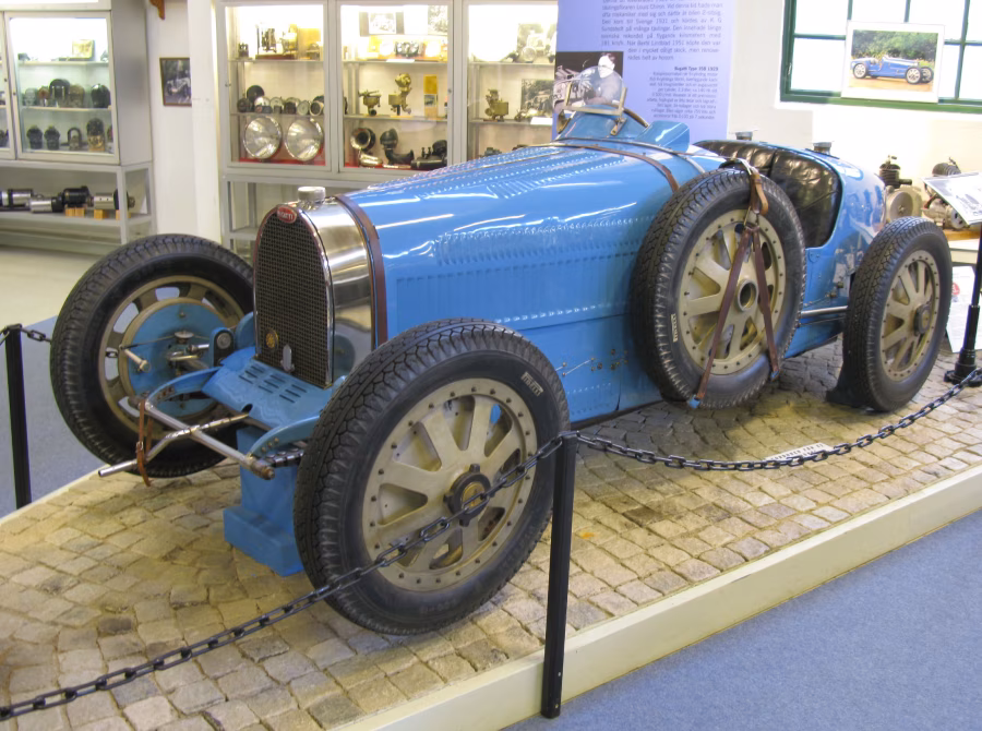 Modré závodní Bugatti Type 35B z roku 1929 s odkrytými koly, koženými řemeny a dvěma sedadly v muzeu