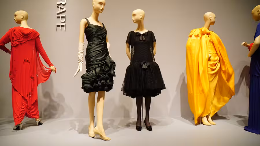 Černé koktejlové šaty Yves Saint Laurent s velkou mašlí stojí uprostřed muzejní instalace mezi modely dalších autorů