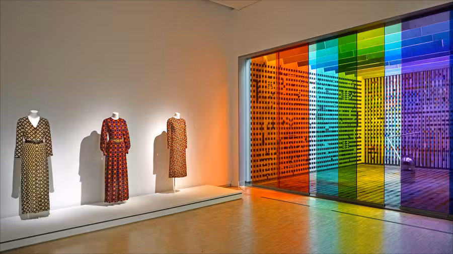 Tři dlouhé vzorované šaty Yves Saint Laurent z let 1968 až 1970 stojí vlevo na podstavci pařížské muzejní expozice