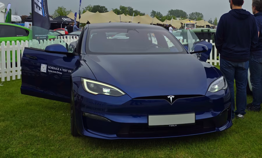 Tmavě modrá Tesla Model S z roku 2024 fotografovaná zepředu s otevřenými dveřmi na venkovní automobilové akci