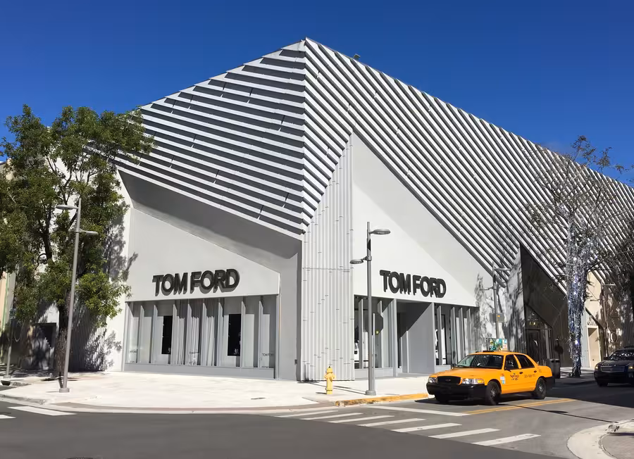 Bílá hranatá budova prodejny Tom Ford v Miami má prosklené průčelí, dvě černá loga a před vchodem stojí žlutý automobil