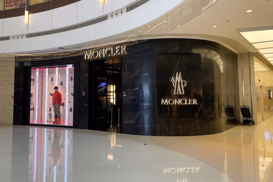 Prosklený butik Moncler v Čeng čou má černé kamenné průčelí, svítící logo a figurínu v červené péřové bundě