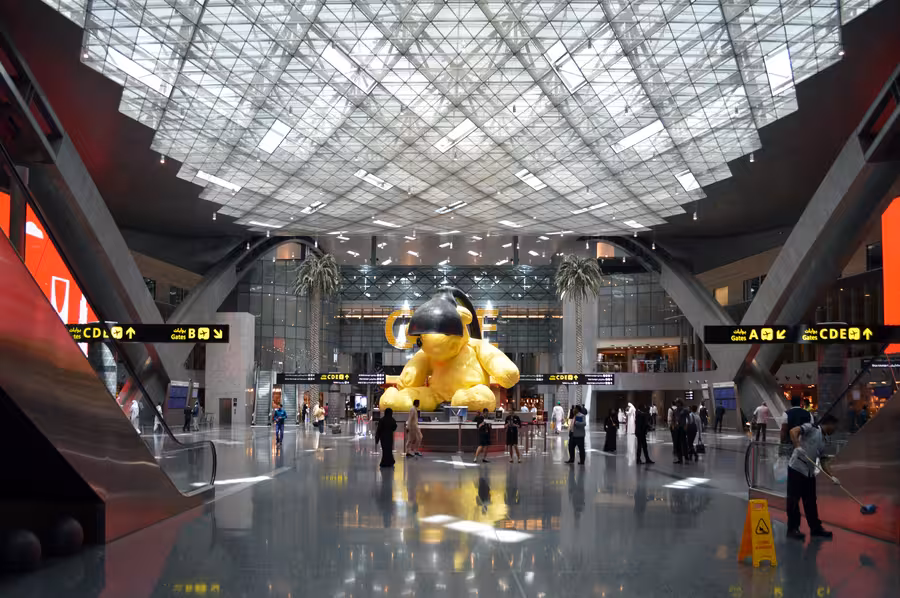 Prostorná hala letiště Hamad International Airport s proskleným stropem a žlutou sochou medvěda