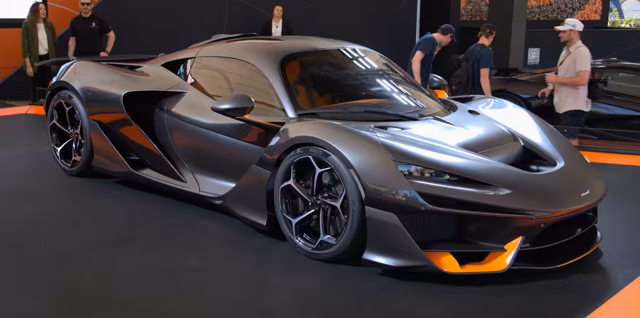 Šedý McLaren W1 s oranžovými detaily vystavený z předního tříčtvrtečního pohledu v pavilonu Festivalu rychlosti v…