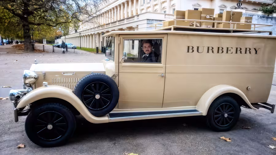 Řidič sedí v krémové dodávce Burberry v historickém stylu s dárkovými krabicemi na střeše na londýnské třídě The Mall