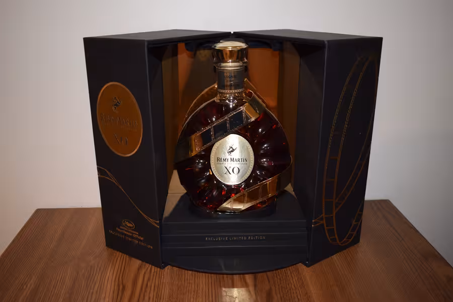 Kulatá karafa Rémy Martin XO s dekorací filmového pásu stojí v černém otevřeném boxu