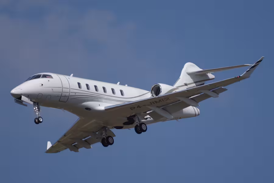 Bílý Bombardier Challenger 3500 s modrými a zlatými pruhy letí s vysunutým podvozkem proti modré obloze