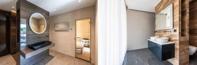 Velkoformátové obklady a dlažby má majitel také v koupelnách. Na fotografii vlevo je na podlaze položena dlažba imitující mramor s názvem Canova. Má rozměr 60x120 cm.  Na stěně je obklad, který se jmenuje Discover ve formátu 60x120 cm. Ostrůvek je vytvořený z dlažby imitující dřevo Chalet, která má rozměr 20x80 cm. Na fotografii vpravo je na podlaze koupelny položena dlažba imitující kámen s názvem Ardesia, která má rozměr 45x90 cm. Ostrůvek je obložen dlaždicemi v rozměru 150x75 cm. 